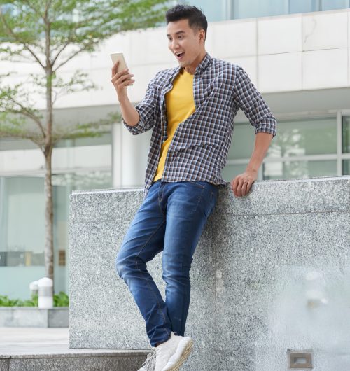AI Enhancer-Ultra HD-full-length-shot-young-handsome-guy-excitied-by-news-read-smartphone